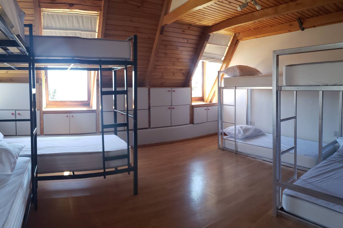 A room with bunk beds, wooden beams, and a window with curtains.