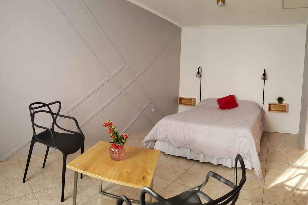 A bedroom with a bed, a table with a vase, two chairs, and a bedside lamp.