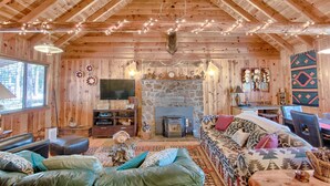 A cozy log cabin interior with a fireplace, wooden walls, and a stone hearth. - Family Cabin in the Pines. All Wood! Charming memory-maker. (Pinetop-Lakeside)