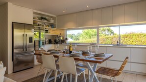 Une cuisine moderne dotée d’un réfrigérateur encastré, d’une table à manger avec assiettes et verres à vin, et d’une fenêtre donnant sur un jardin.
