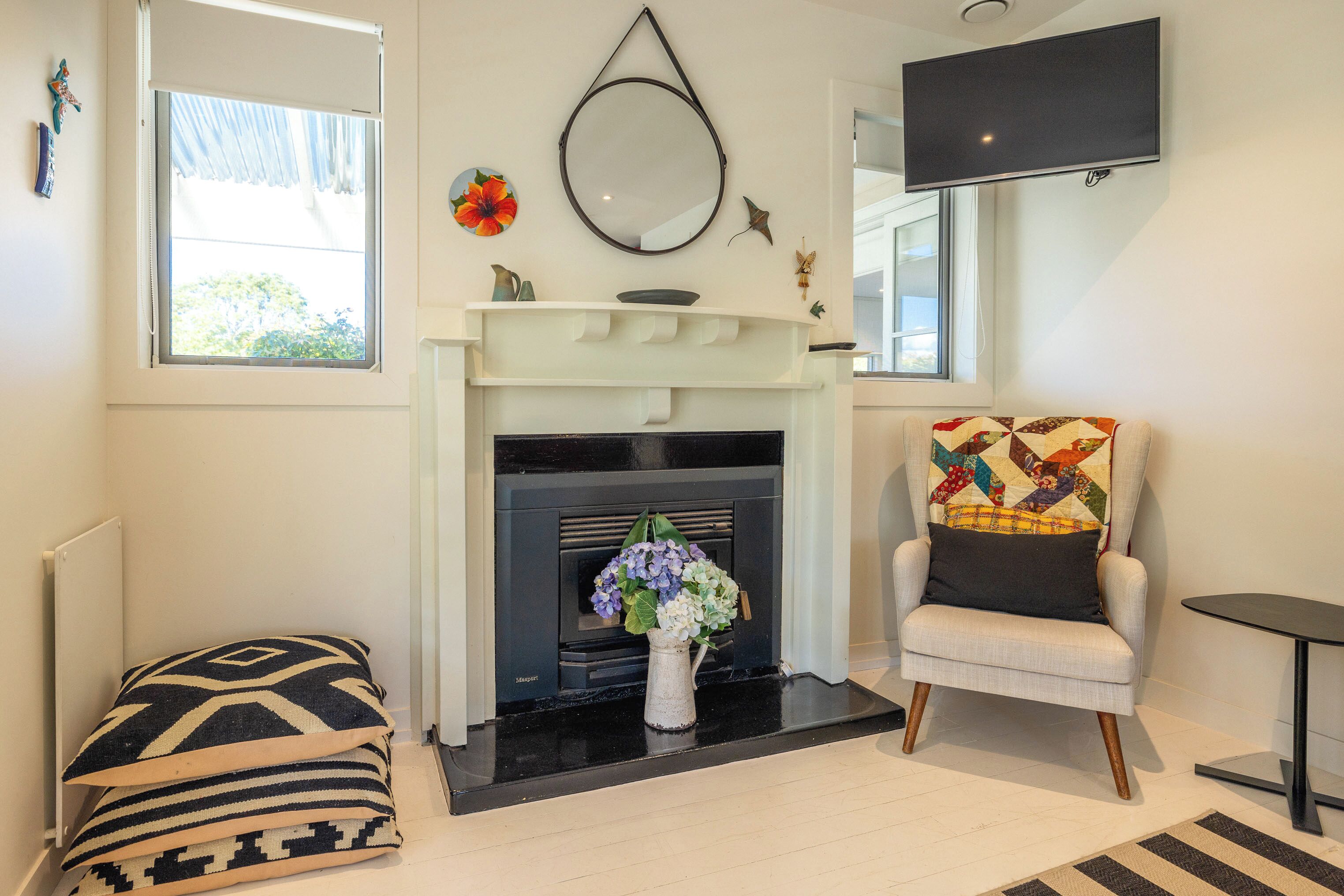 A living room with a fireplace, a comfortable armchair, a small table, and a decorative mirror.