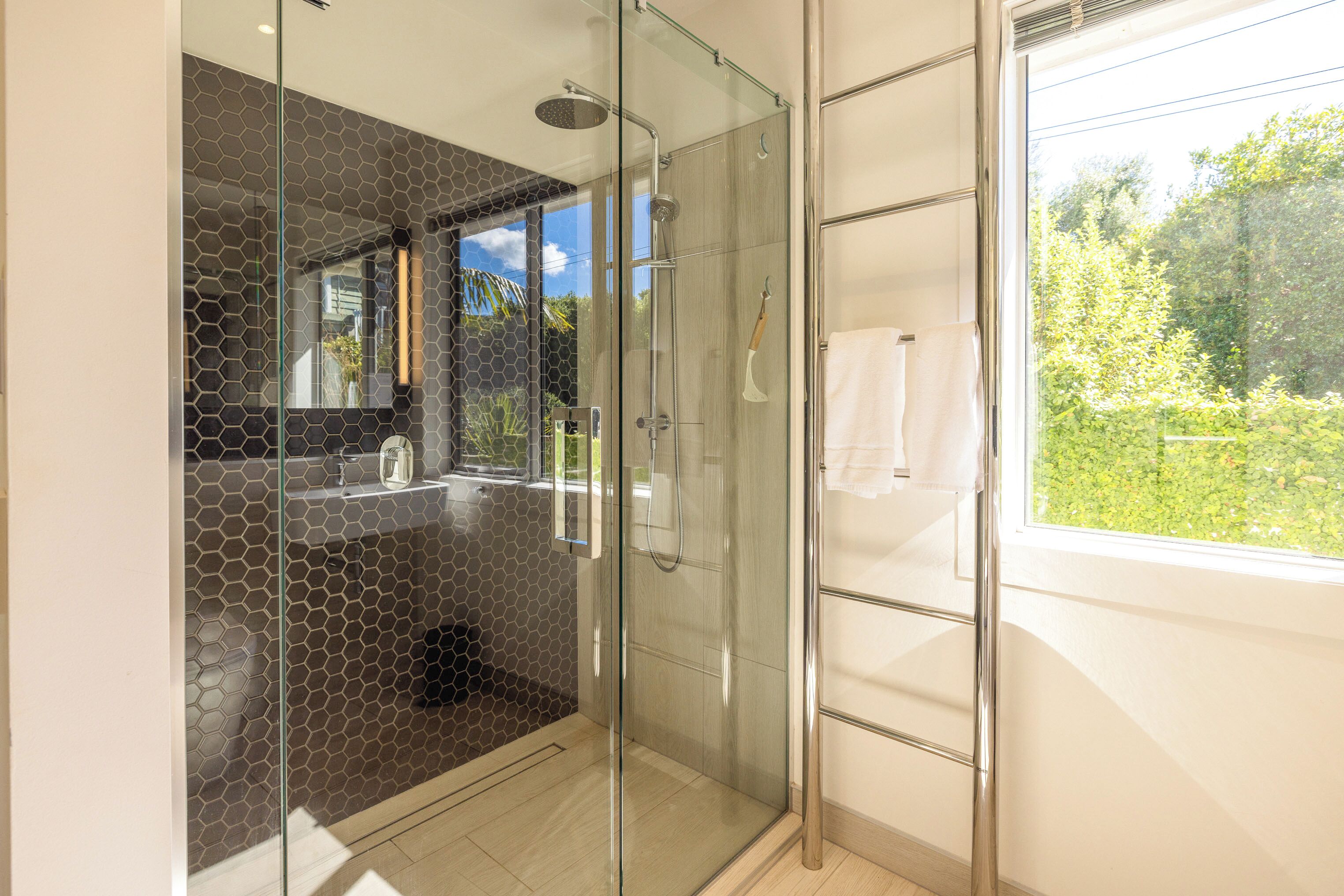Une salle de bain moderne dotée d’une douche à parois de verre, d’un lavabo apparent et d’une fenêtre donnant sur un paysage verdoyant.