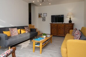 A living room with a grey sofa, yellow sofa, wooden coffee table, and a TV on a wooden cabinet. - Amodo Lodge - JARO Room (Saint-Paul-en-Chablais)
