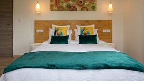 Een net opgemaakt bed met een groene deken, twee sierkussens met bloemmotieven, en een houten hoofdbord.