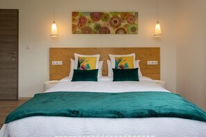 A neatly made bed with a green blanket, two pillows with floral designs, and a wooden headboard. - Amodo Lodge - JARO Room (Saint-Paul-en-Chablais)