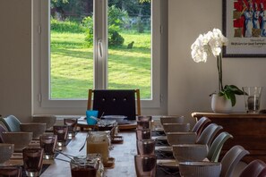 A dining area with a view of a grassy yard, a table set with various dishes and glasses, and a framed artwork on the wall. - Amodo Lodge - JARO Room (Saint-Paul-en-Chablais)