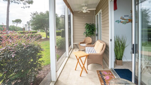 A covered porch with wicker furniture, a ceiling fan, and a view of a landscaped garden. - Sandpiper 2A Sunset Beach (Sunset Beach)