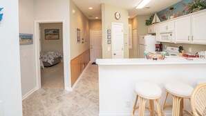 A kitchen with white cabinets, a white countertop, and a clock on the wall. - Sandpiper 2A Sunset Beach (Sunset Beach)