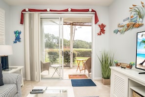 Una habitación con puerta corrediza de vidrio que da a un patio, un sofá blanco, una mesita, un televisor y un cartel de 'No Smoking'.