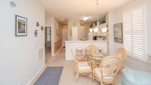 A dining area with wicker chairs, a glass table, and a chandelier. - Sandpiper 2A Sunset Beach (Sunset Beach)