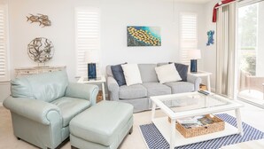 A living room with a light blue sofa, a striped sofa, a glass coffee table, and a white side table with a lamp. - Sandpiper 2A Sunset Beach (Sunset Beach)