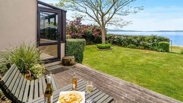 Eine Terrasse mit Tisch, gedeckt für eine Mahlzeit, einer Weinflasche und einem Glas.