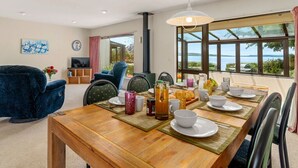 Ein Essbereich mit einem Holztisch, gedeckt für das Frühstück, einem blauen Sessel und Blick auf den See.
