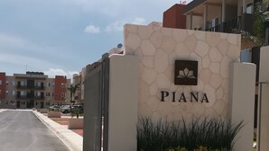 L'ingresso di un edificio con un cartello che riporta la scritta "PIANA" e un muro in pietra con un'antenna parabolica.