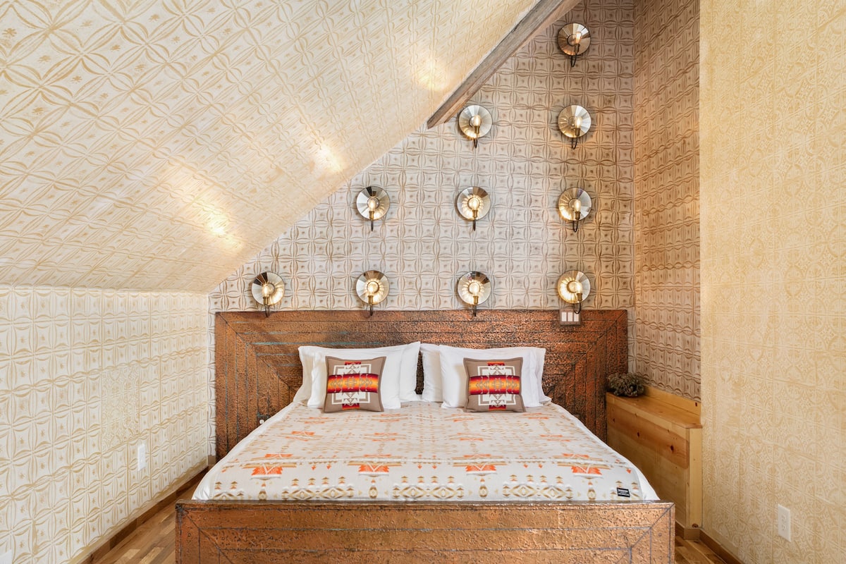 A bedroom with a patterned ceiling, a wooden headboard, and wall-mounted lights.