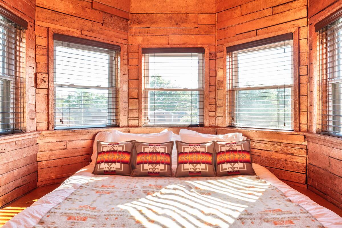 A wooden cabin-style bedroom with a bed, pillows, and a window with blinds.