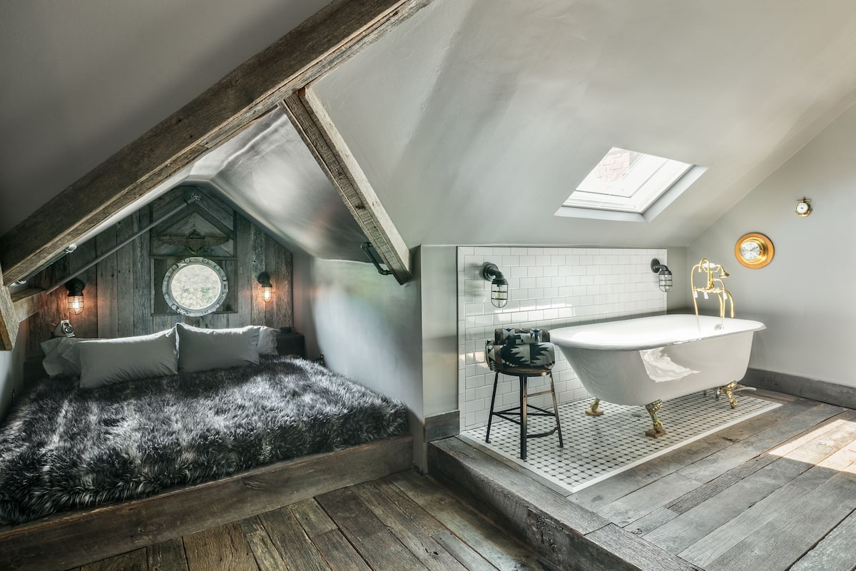 A bedroom with a sloped ceiling, a large window, and a rustic wooden beam structure.