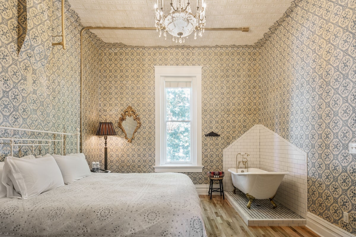 A bedroom with a bed, a vanity with a mirror, and a bathtub.