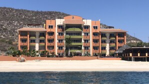 A multi-story hotel with balconies, located on a beach with a view of the sea.