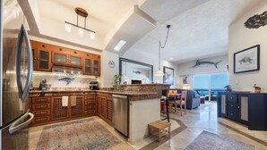 A spacious kitchen with wooden cabinets, a large refrigerator, and a dining area with a view of the ocean.