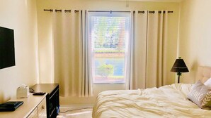 Une chambre à coucher avec un lit, un bureau avec une lampe et une fenêtre avec des rideaux.