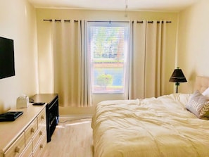 A bedroom with a bed, a desk with a lamp, and a window with curtains.
