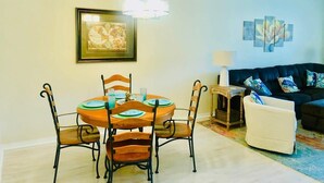 Un coin repas avec une table ronde, quatre chaises, un lustre et un tableau au mur.