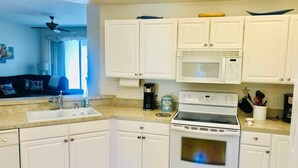 Une cuisine avec des meubles blancs, une cuisinière, un four à micro-ondes et un évier.