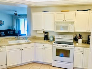 A kitchen with white cabinets, a stove, a microwave, and a sink.