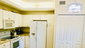 Une cuisine de taille réduite avec des meubles blancs, un four à micro-ondes, une cuisinière, un réfrigérateur et un luminaire fixé au plafond.
