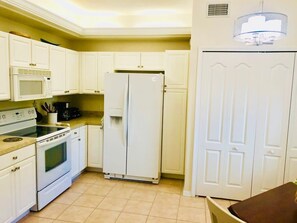 A compact kitchen with white cabinets, a microwave, stove, refrigerator, and a ceiling light fixture.