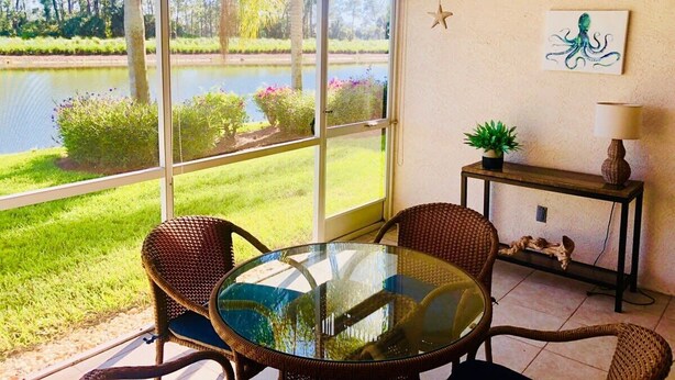Une pièce avec une table en verre, des chaises en osier, une petite console sur laquelle est posée une lampe, et un tableau représentant une pieuvre accroché au mur.