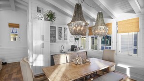 A dining area with a wooden table, cushioned chairs, and a bench. There are two hanging crystal chandeliers. - Buckeye on the Beach | Gulf Front | Seaside, FL | Right next to Town Center, Sleeps 10! (Santa Rosa Beach)