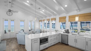 A modern kitchen with white cabinetry, a central island, and a view of the ocean. - Buckeye on the Beach | Gulf Front | Seaside, FL | Right next to Town Center, Sleeps 10! (Santa Rosa Beach)
