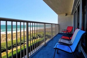 A balcony with a view of the beach, two red and one blue chair, and a concrete floor. - Water's Edge - Ocean Front, Indoor/Outdoor Pool, Spa (Carolina Beach)