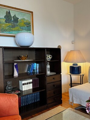 Ein Zimmer mit einem dunklen Holzregal, einer weißen Vase, einer blauen Lampe und einem Gemälde an der Wand.