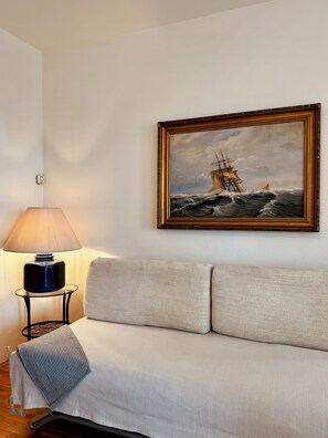 Ein Zimmer mit einer Couch, einer Lampe und einem gerahmten Gemälde eines Schiffes auf dem Meer.