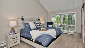A bedroom with a bed, bedside tables, a lamp, and a window with a view of trees.
