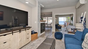 A modern living room with a blue sofa, a flat-screen TV, and a kitchen area with wooden cabinets and a dining table.