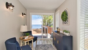 A room with a view of the beach, a dark-colored cabinet, a lamp, and a blue chair.