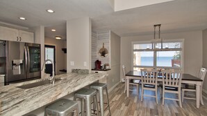 A modern kitchen with a marble countertop, stainless steel appliances, and a dining area with wooden chairs and a table.