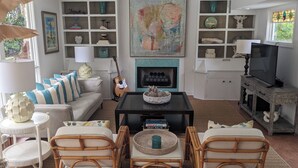 Un salon comprenant un canapé, deux fauteuils en osier, une table basse, une cheminée et un téléviseur.