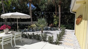 Een terras met een tafel, stoelen, een witte parasol en diverse planten.