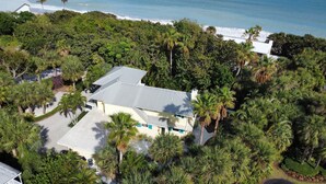 Une vue aérienne d’une maison entourée d’une végétation tropicale luxuriante, avec une plage visible au loin.