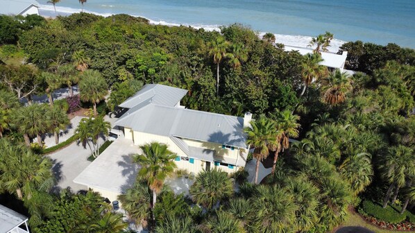 Luchtbeeld van een huis, omringd door weelderige tropische begroeiing, met een strand in de verte.