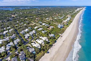 Luchtbeeld van een kustgebied met woningen, een strand en een heldere blauwe oceaan.