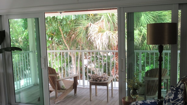 Une pièce dotée d’une porte-fenêtre coulissante donnant sur une terrasse aménagée avec du mobilier d’extérieur et offrant une vue sur la végétation tropicale.