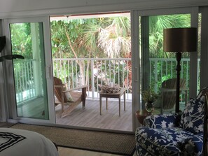 Ein Zimmer mit einer Schiebeglasdoor zum Balkon mit Gartenmöbeln und Blick auf üppige tropische Vegetation.