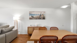 A dining area with a wooden table and wicker chairs, a white sofa, and a painting of a beach scene on the wall.