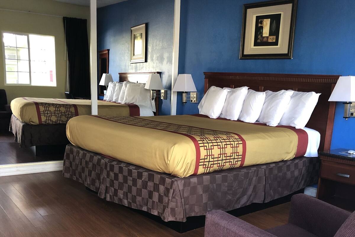 A hotel room with two beds, wooden flooring, and a purple armchair.